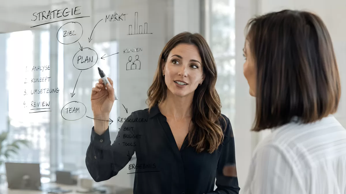 Zwei Frauen besprechen Strategie an Glaswand im Büro