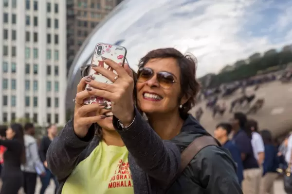 Zwei Frauen lächeln und machen ein Selfie vor dem Cloud Gate vom Künstler Anish Kapoor in Chicago