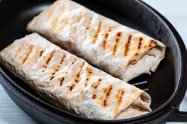 Zwei gerollte Fladenbrote (Shawarma) werden in Pfanne gebraten vor weißem Hintergrund