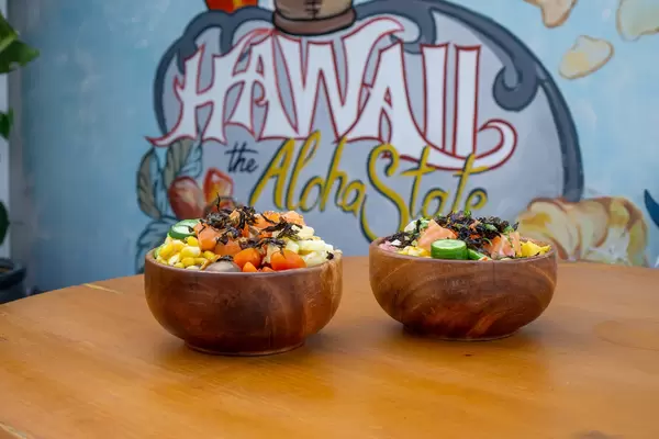 Zwei Gesunde Hawaiianische Poke Bowls auf einem Holztisch mit Hawaii the Aloha State Kunst im Hintergrund