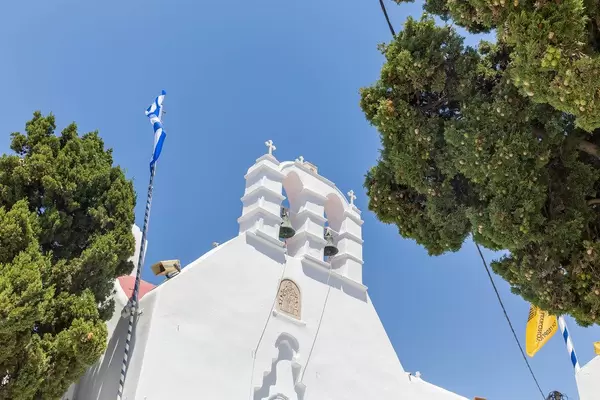 Zwei Glocken, griechische Fahne, Bäume und blauer Himmel. Kirche auf Mykonos