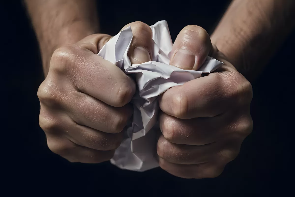 Zwei Hände zerknüllen wütendes Papier vor dunklem Hintergrund