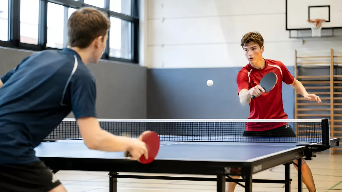 Zwei Jugendliche spielen Tischtennis in einer Sporthalle