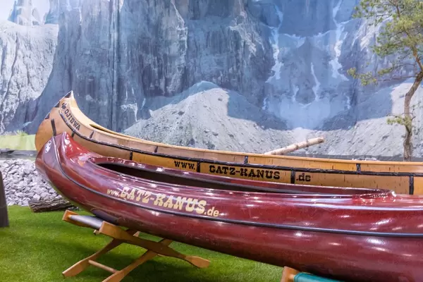Zwei Kanus auf Kunstwiese vor Hintergrund mit Bild von Bergen und Felsen mit Fluss