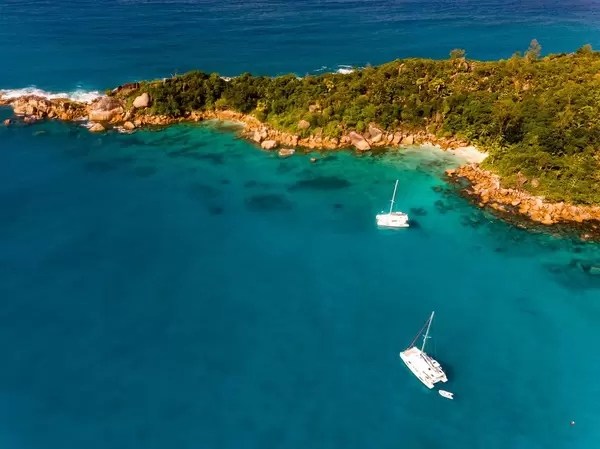 Zwei Katamaran-Boote neben einer Inselzunge an der Nordküste von Praslin, umgeben vom Tiefblauen Meer der Seychellen