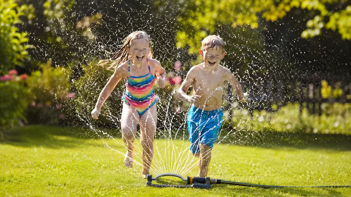 Zwei Kinder lachen beim Spielen am Gartensprinkler