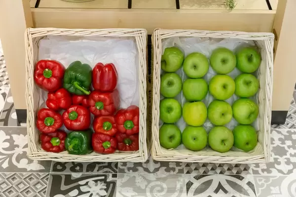 Zwei Körbe mit grünen Äpfeln und Paprika auf gefliestem Boden an Wand gestützt