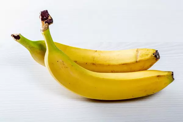 Zwei leuchtend gelbe, ganze Bananen auf weißem Holztisch