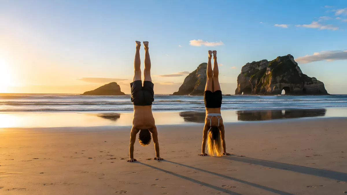 Zwei Menschen beim Handstand am Strand im Sonnenuntergang