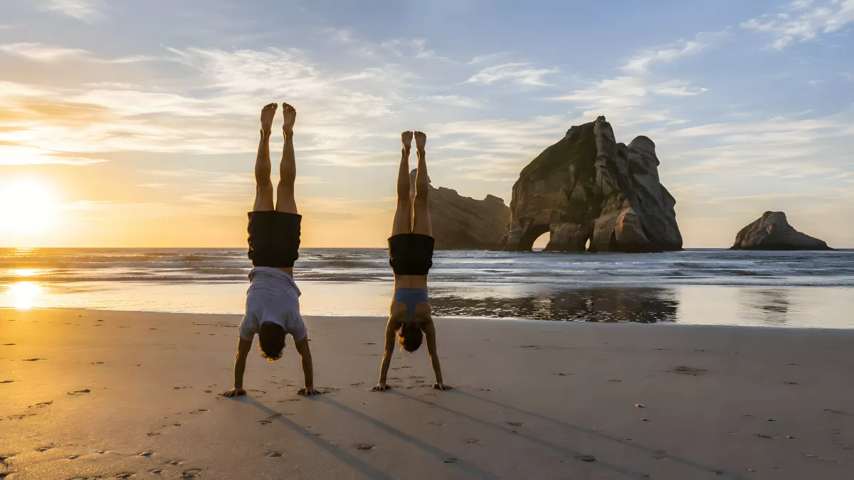 Zwei Menschen im Handstand am Strand bei Sonnenuntergang