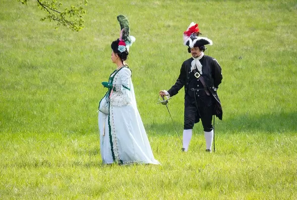 Zwei Menschen in barocken Kleidern in einem Schlosspark