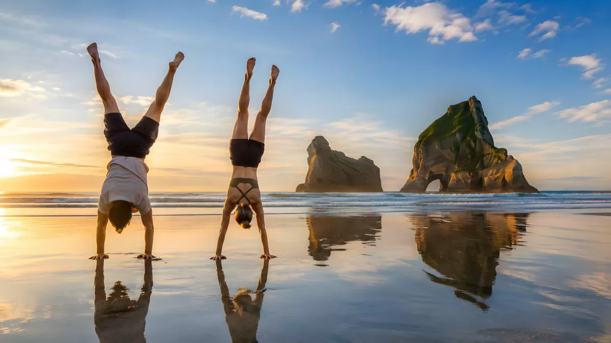 Zwei Personen beim Handstand am Strand im Abendrot