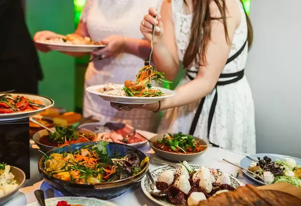 Zwei Personen stehen mit Tellern vor einem Buffet mit verschiedenen Gerichten