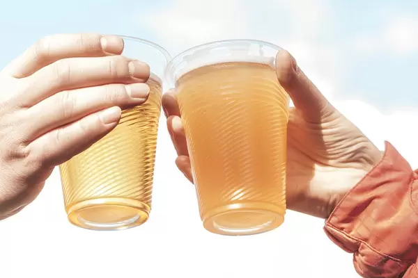 Zwei Plastikbecher mit Bier in Frauenhänden mit Himmel-Hintergrund