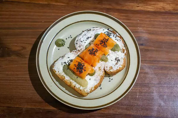 Zwei Scheiben Weißbrot mit Frischkäse, Gewürzgurken, Räucherlachs und schwarzen Sesamkörnern von oben fotografiert