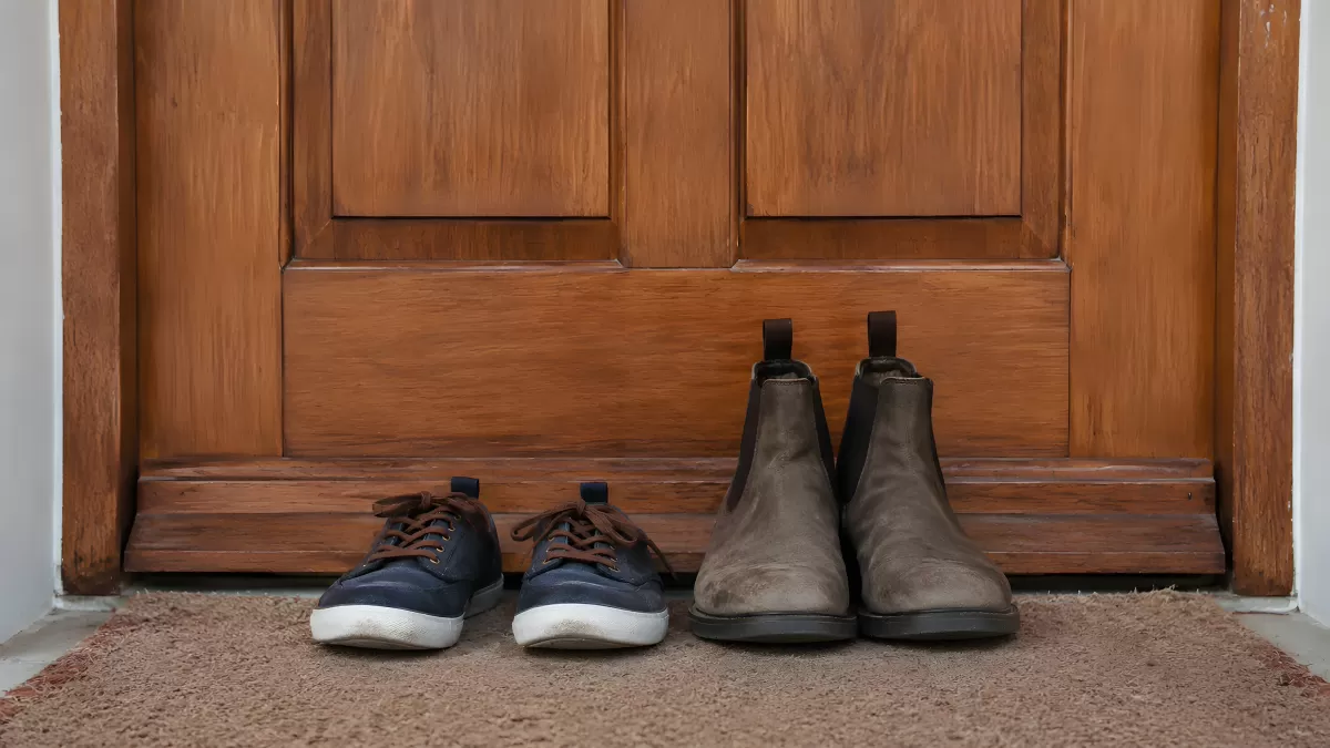 Zwei Schuhpaare vor einer Holztür auf Fußmatte