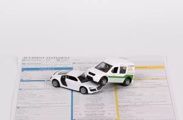 Zwei Spielzeugautos auf einer noch nicht vervollständigten Unfallschadenmeldung