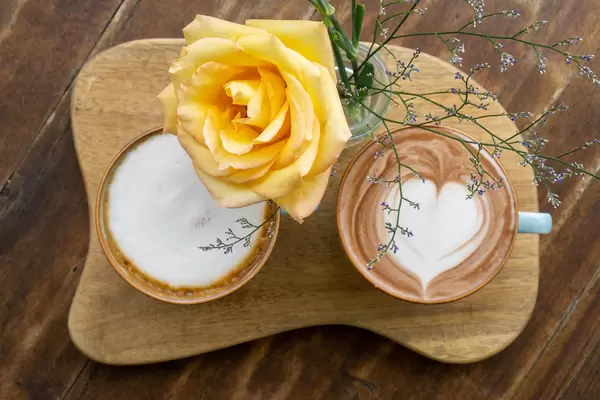 Zwei Tassen mit heißer Schokolade und Cappuccino mit Latte Art Herz von oben auf einem Holzbrett mit Blume fotografiert