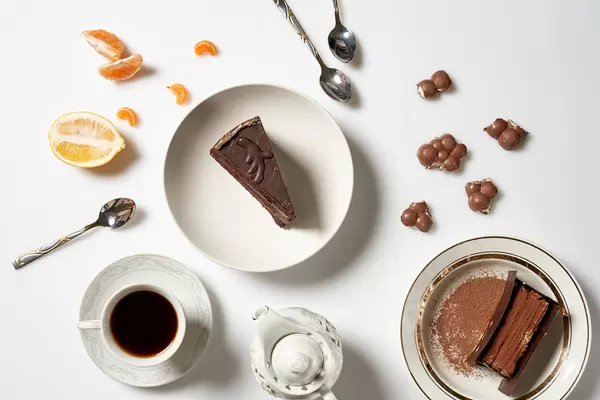 Zwei Teller mit jeweils einem Tortenstück, eine Tasse Kaffee, Schokolade, Zitrone, Mandarine, Kanne, Löffel