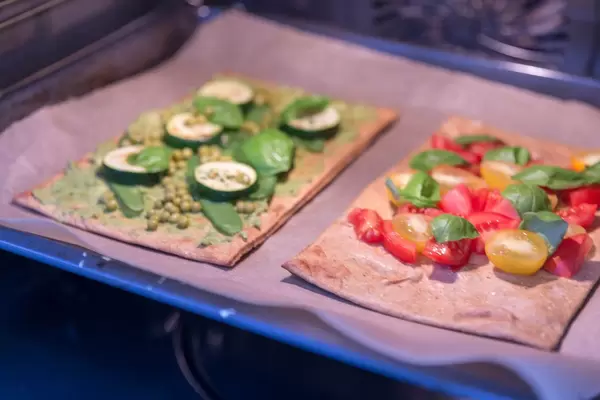 Zwei vegane Pizzen mit frischen Zutaten belegt im Ofen