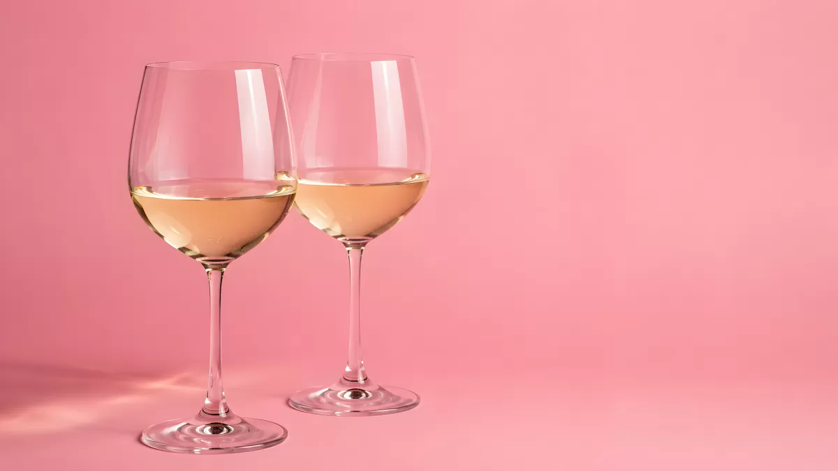 Zwei Weingläser mit Weißwein vor rosa Hintergrund