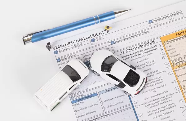 Zwei weisse Spielzeugautos und ein Kugelschreiber auf Versicherungsunterlagen für die Meldung von einem Autounfall