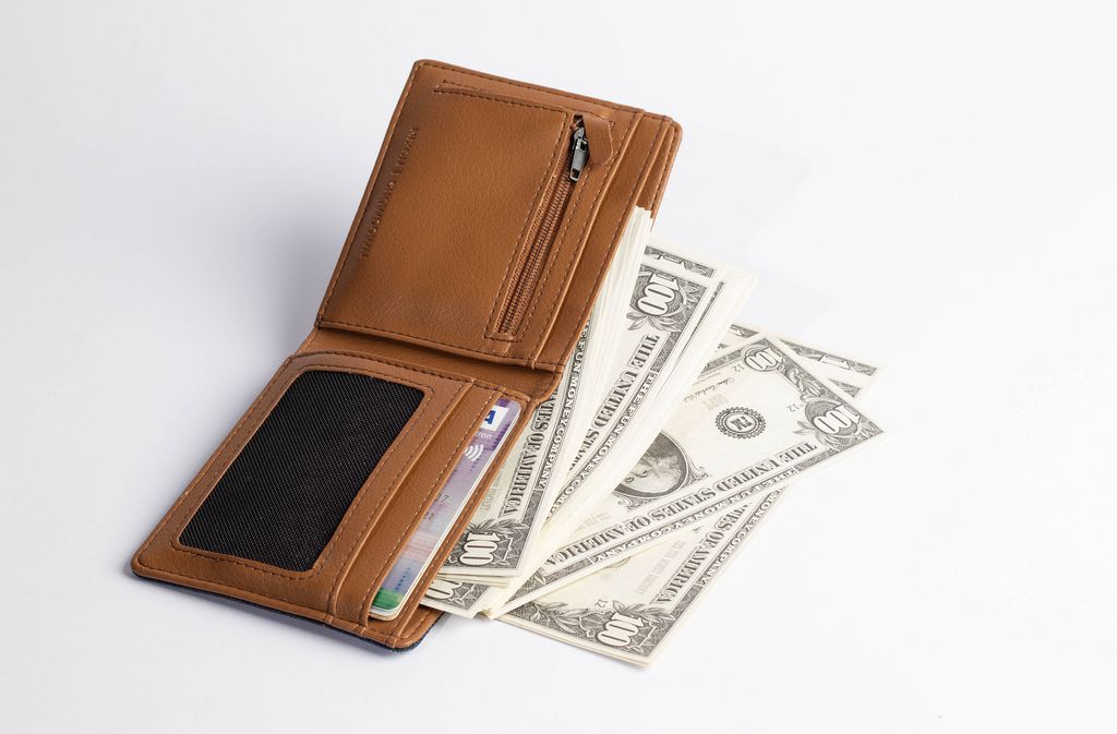 100-Dollar Banknoten fallen aus geöffneter Brieftasche aus braunem Leder vor weißem Hintergrund