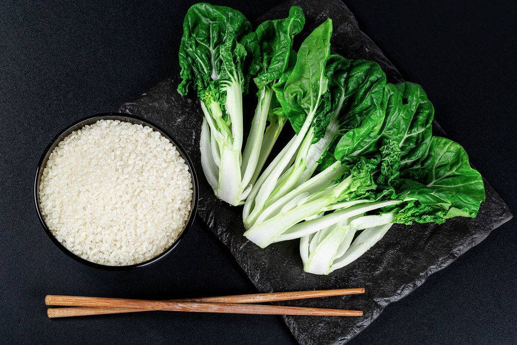A bowl of rice, chopsticks and cabbage Pak Choi baby on a black background, top view