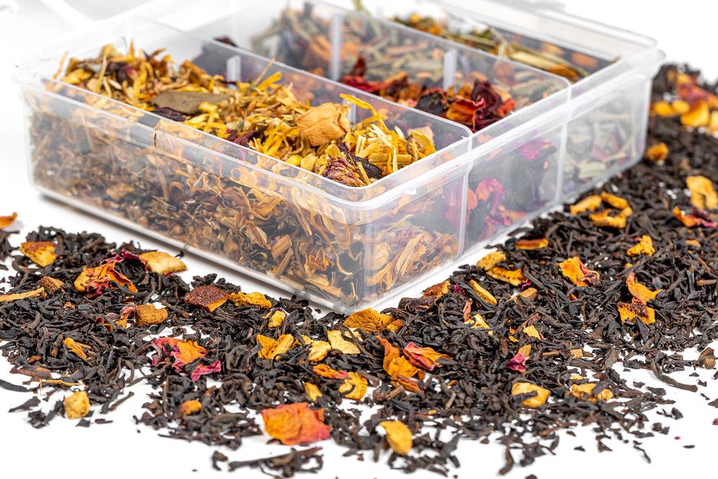 A box with different types of tea and scattered dry tea on a white background