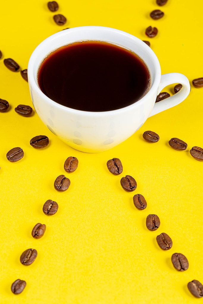 A Cup of fresh coffee on a yellow background and coffee beans