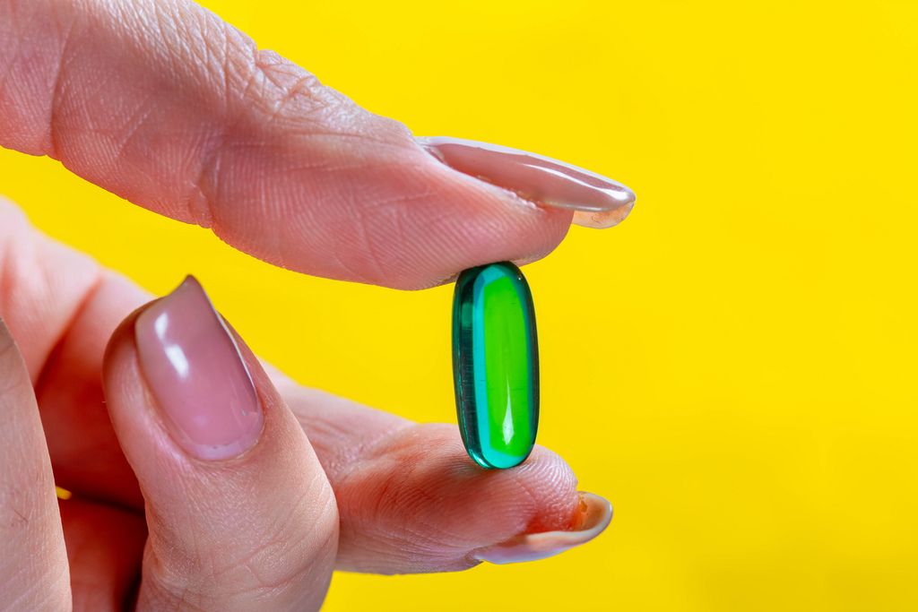 A girl holds a capsule of painkillers in hand on yellow background