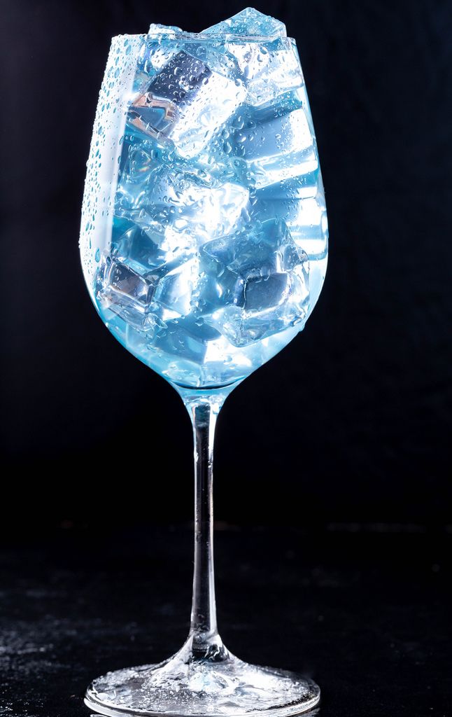 A glass filled with a blue cocktail with ice on black background