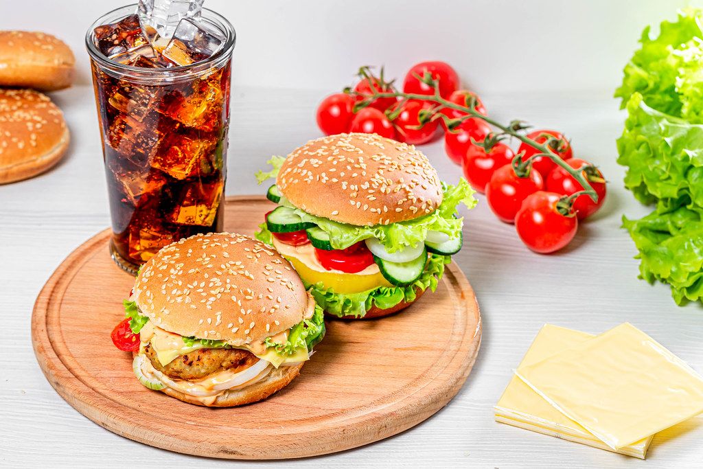 A glass of Cola with ice and fresh burgers on a round kitchen Board (Flip 2019)