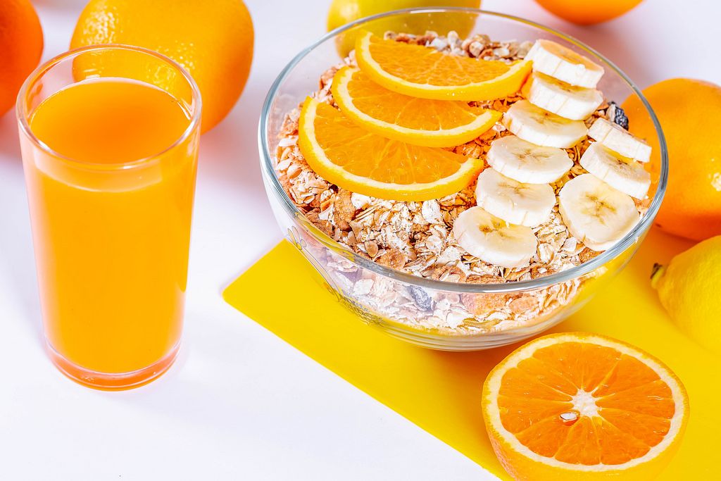A glass of fresh orange juice and a bowl of dietary porridge with oranges and bananas