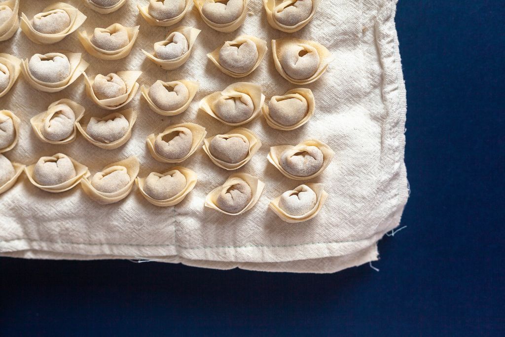 A large number of dumplings in several rows laid out on white textile.