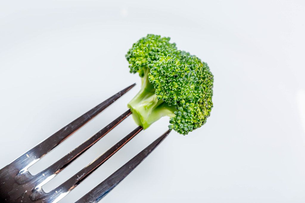 A piece of fresh broccoli on a fork on a white background