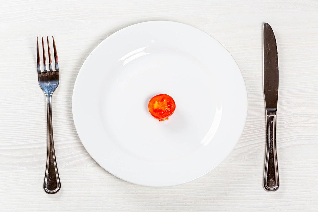 A piece of tomato on a white plate with a knife and fork. Weight loss concept