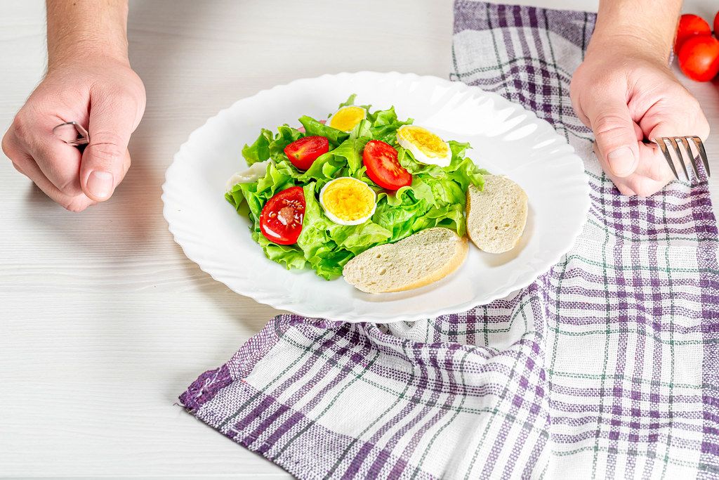 A plate of fresh salad and a man's hands with a knife and fork