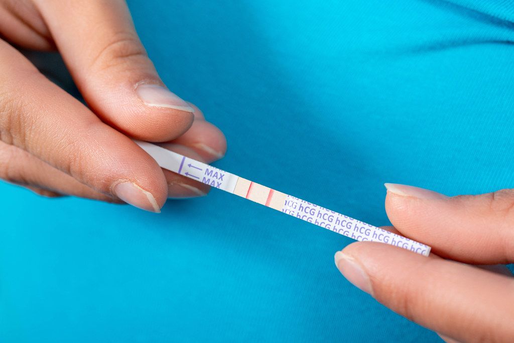 A woman holds a positive pregnancy test with two stripes