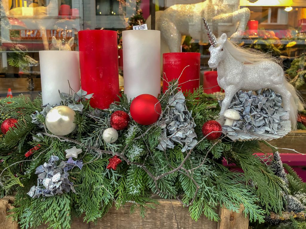 Adventskranz aus Tannenzweigen mit roten und weißen Kerzen, Weihnachtskugeln und Sternen und einem glitzernden Einhorn