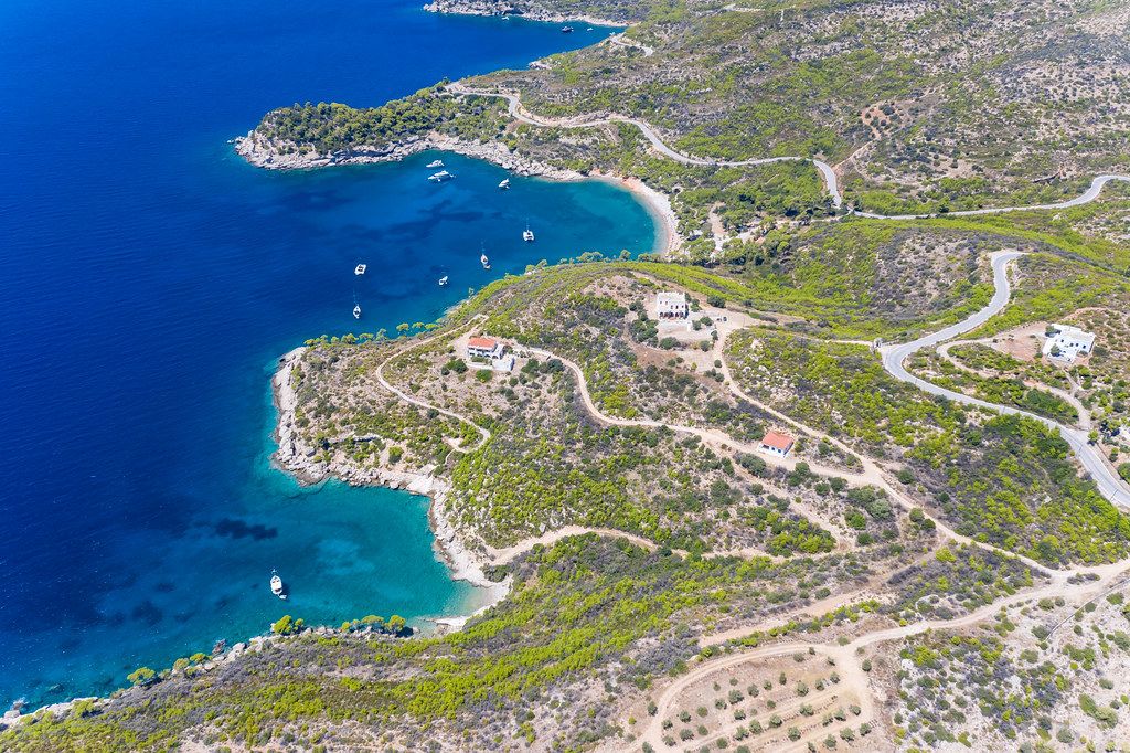 Aerial picture of single houses on the greek island Spetses, with its rocky coasts and boats on the blue sea