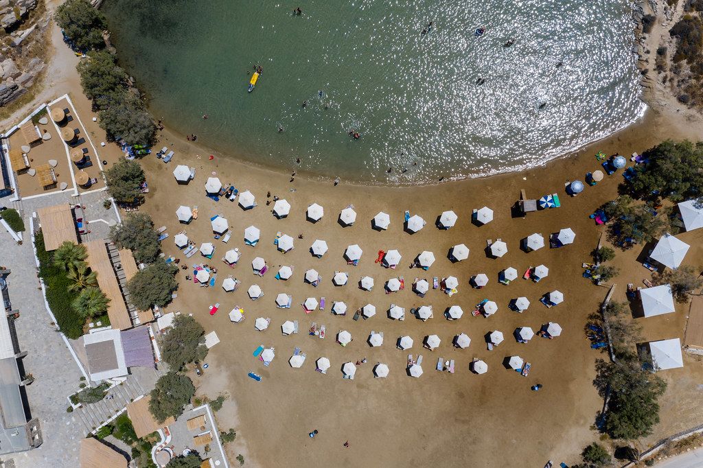Aerial shot of white parasols, lined up on a sandy beach at the Aegean Sea at Paros, Greece