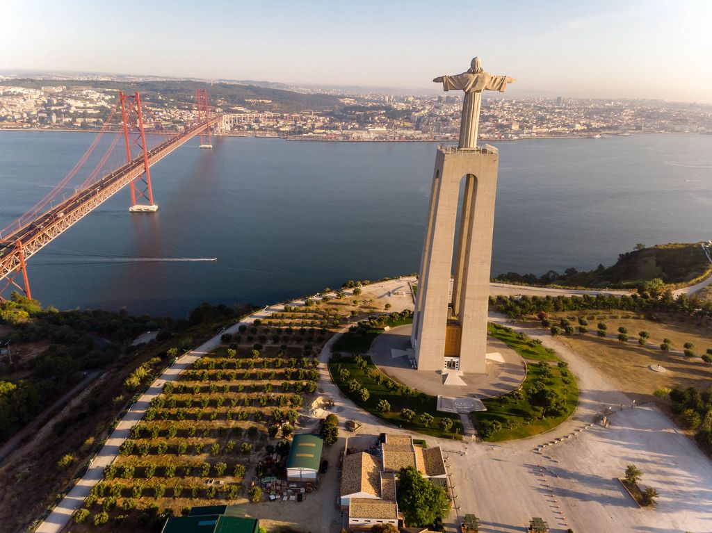 Aerial view drone shot from behind of the Cristo Rei monument with Ponte 25 de abril bridge in Almada Lisbon