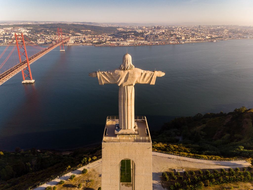 Aerial view from behind of the Cristo Rei statue in Almada, looking over the Tajo river with Ponte 25 de Abril bridge