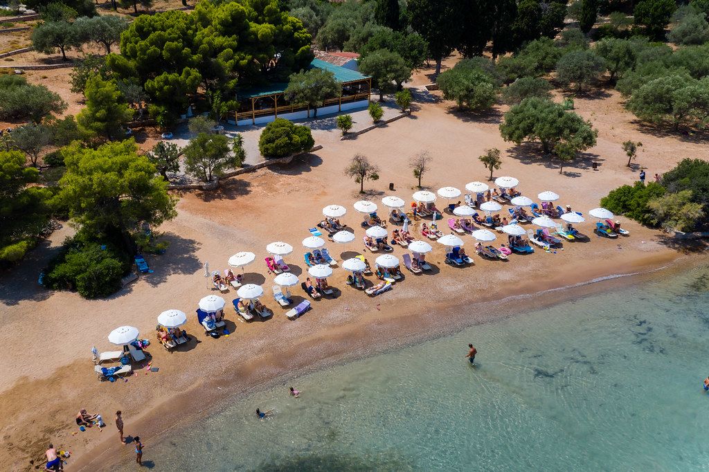 Aerial view of the white sandy beach with sunshades and beach chairs, in front of the Zogeria restaurant & beach bar on Spetses, Greece