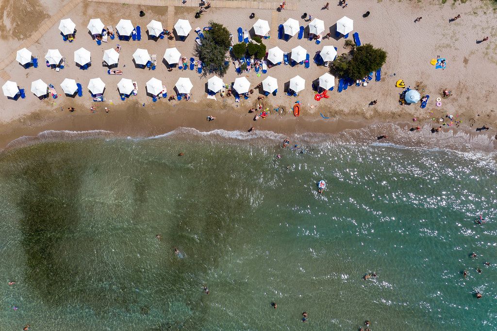 Aerial View Of Tourists And Families On Vacation At A Public Beach With Colorful Dinghy