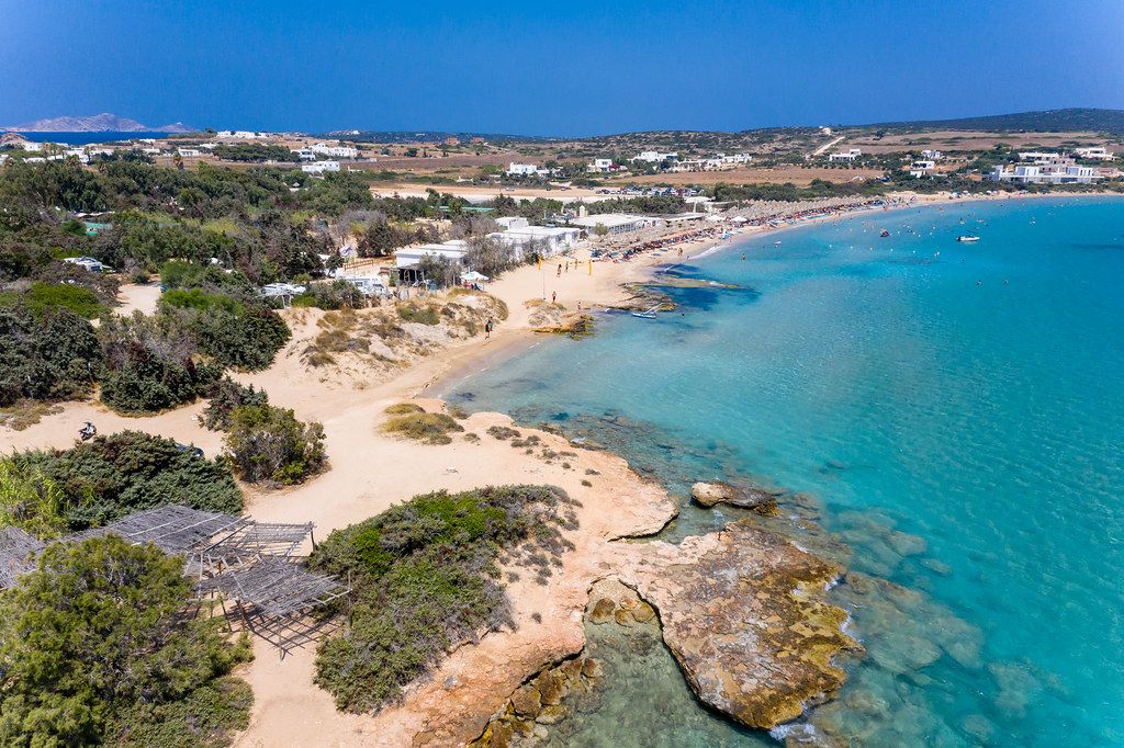 Aerial view of tourists on vacation at the Santa Maria Beach with beach bar and swimming people in the Mediterranean Sea in front of the Greek island Paros