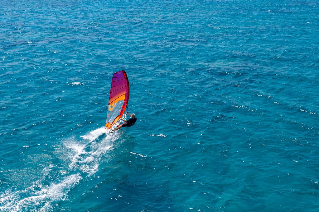 Aerial view shows a water sportsman windsurfing in the blue Mediterranean Sea, in front of Santa Maria Beach on Paros, Greece