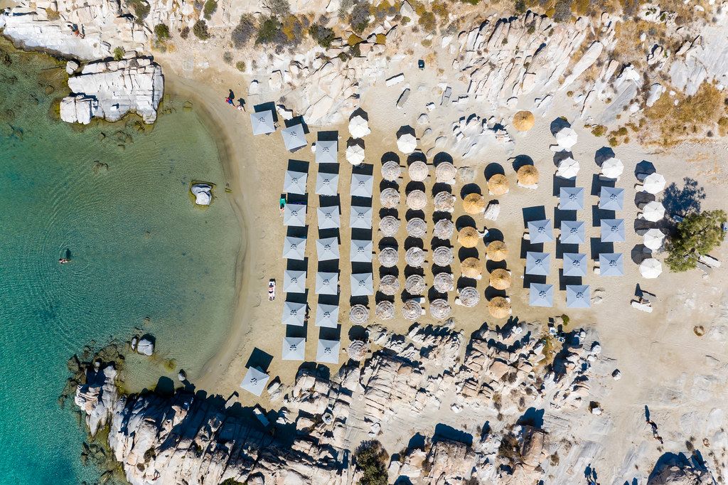 Aerial view shows the rocky beach in Kolympithres on Paros, with parasols on the white sandy beach at the green Mediterranean Sea