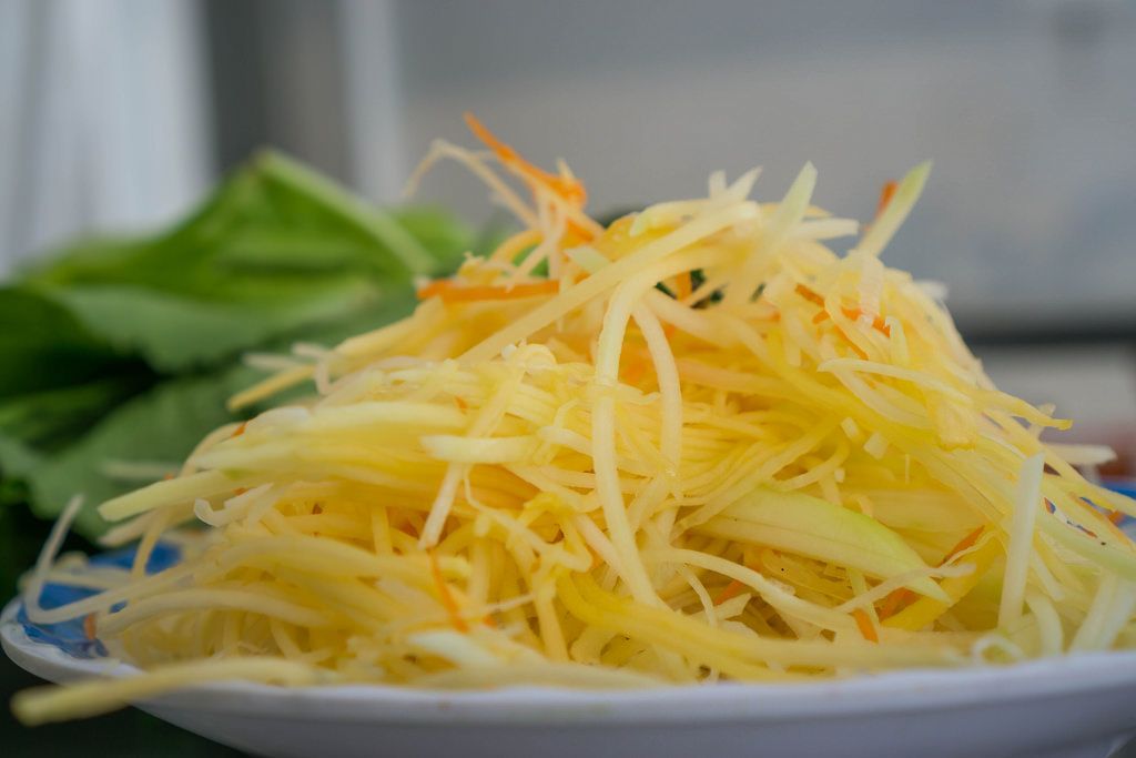 Als Beilage servierte, in dünne Streifen geschnittene grüne Papaya auf weißem Teller mit Salatblatt im Hintergrund